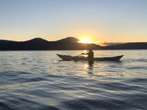 A person kayaking on calm water at sunset, with mountains silhouetted in the background.