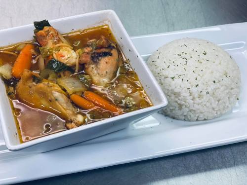 A bowl of chicken soup with vegetables, served alongside a mound of white rice on a rectangular plate.