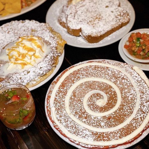 A table filled with desserts, including a spiral cake, a fried pastry with ice cream, and a colorful salsa.