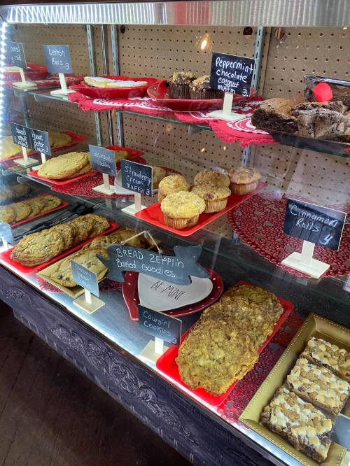 A display case filled with various baked goods, including cookies, muffins, and brownies, labeled with prices.