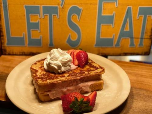 A plate of French toast topped with whipped cream and strawberries, with a colorful "Let's Eat" sign in the background.