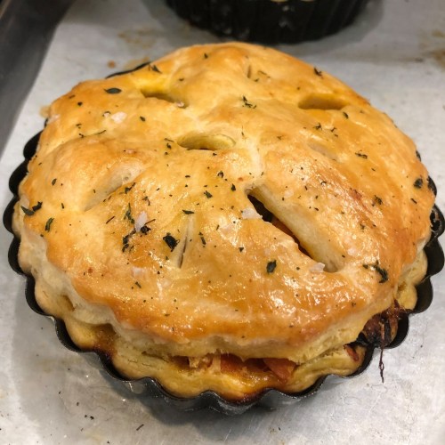 Golden-brown pie in a black tart pan, with a flaky crust and decorative slits on top, resting on a baking sheet.