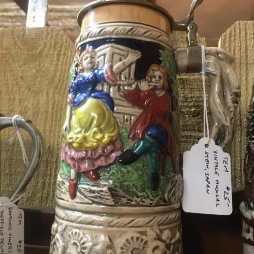 Ceramic stein featuring colorful relief figures of a man and woman in traditional attire, set against a rustic background.