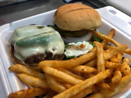 A plate with a cheeseburger topped with jalapeños and a side of crispy French fries.