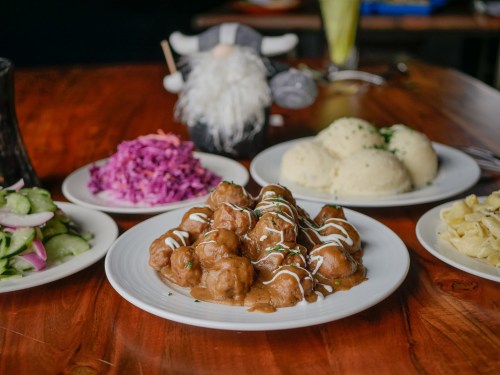 A plate of meatballs in sauce, surrounded by sides of mashed potatoes, purple cabbage, and a cucumber salad.