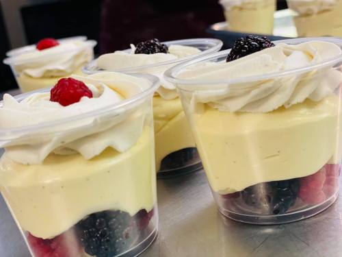 Four dessert cups layered with cream, berries, and topped with whipped cream and a raspberry.