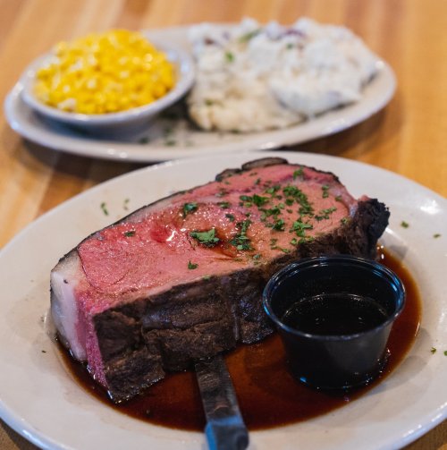 A plate featuring a slice of prime rib with a side of au jus, garnished with parsley, and bowls of macaroni and mashed potatoes.