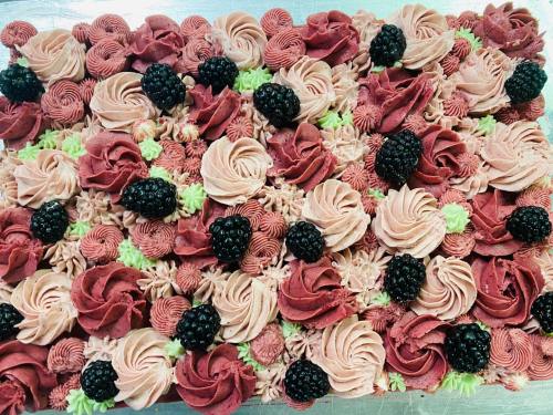 A colorful cake decorated with swirls of pink and green frosting, topped with blackberries and intricate piping.