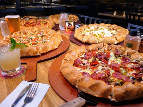 A table with four pizzas featuring stuffed crusts, alongside drinks and condiments in a cozy restaurant setting.