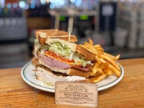 A stacked sandwich with ham, turkey, lettuce, and tomato, served with fries, on a plate at Berry Fields Cafe.