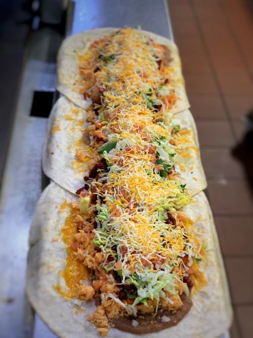 A long burrito filled with rice, beans, chicken, lettuce, and cheese, placed on a countertop.