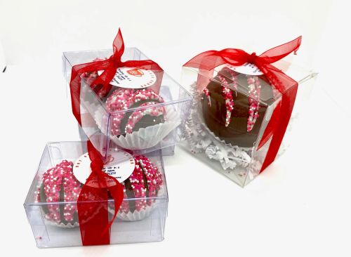 Three chocolate-covered treats in clear boxes, decorated with pink and white sprinkles, tied with red ribbons.
