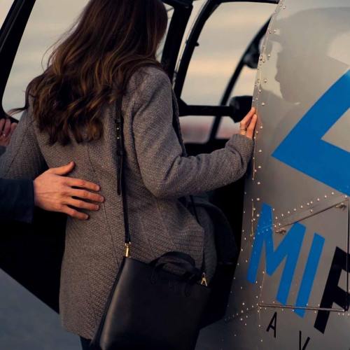 A person with long hair is boarding a helicopter, while another person gently places a hand on their back.