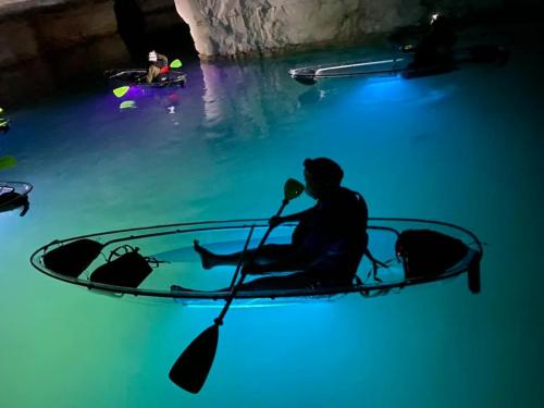 A person in a kayak with a glowing paddle, surrounded by others in illuminated kayaks on a serene, blue-lit water.