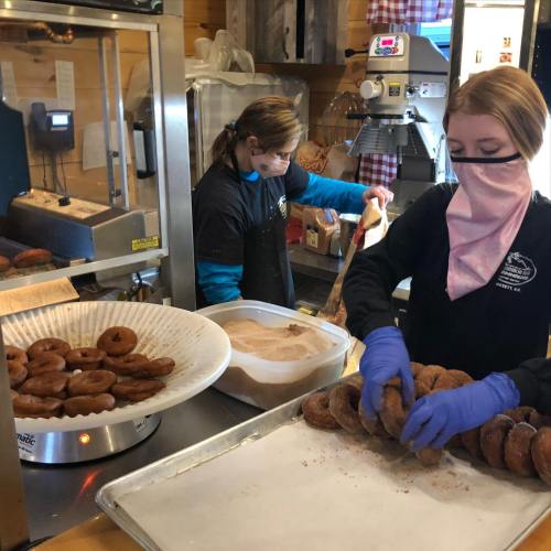 Two workers in a bakery prepare and coat freshly made donuts with cinnamon sugar.
