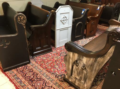 A collection of wooden church pews in various styles, arranged on a decorative rug.