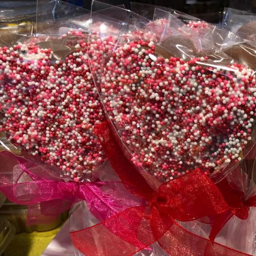 Heart-shaped cookies covered in pink, white, and red sprinkles, wrapped in clear plastic with a pink ribbon.