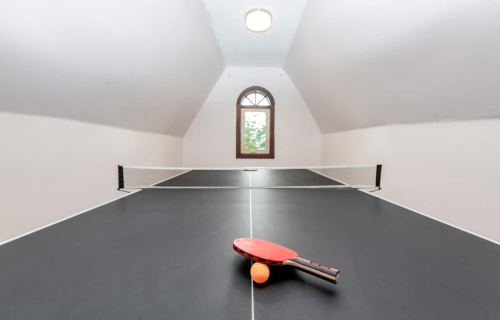 A ping pong table in a bright, airy room with a paddle and ball resting on the surface.