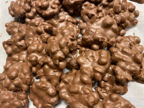 A close-up of clusters of chocolate-covered treats, resembling small, irregularly shaped blobs, on a white surface.