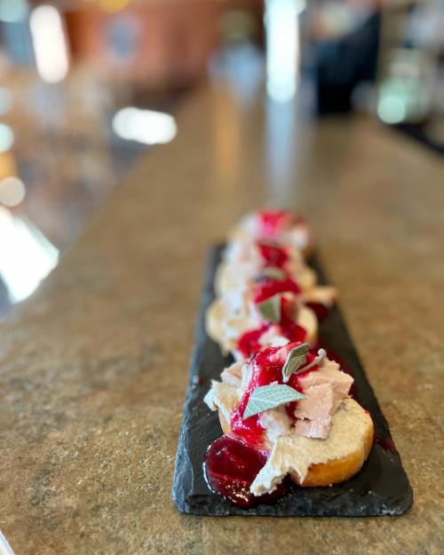 A platter of small appetizers featuring creamy spread, garnished with sauce and herbs, on a dark slate board.