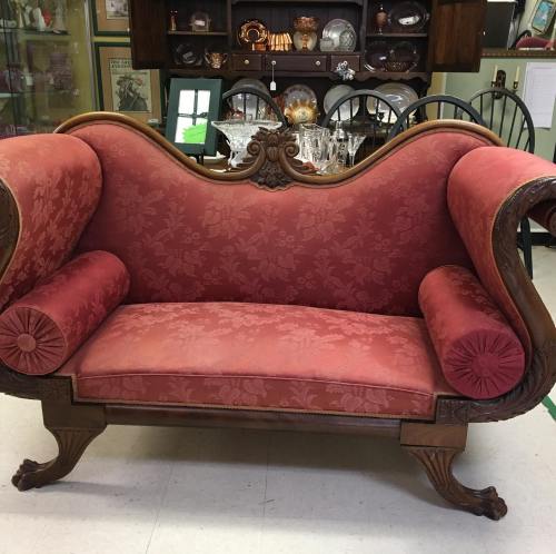 Antique red upholstered loveseat with ornate wooden details and curved arms, set in a vintage decor environment.