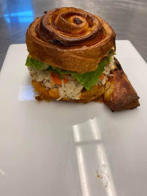 A sandwich featuring a spiral bread roll filled with chicken, lettuce, and vegetables, served on a white plate.
