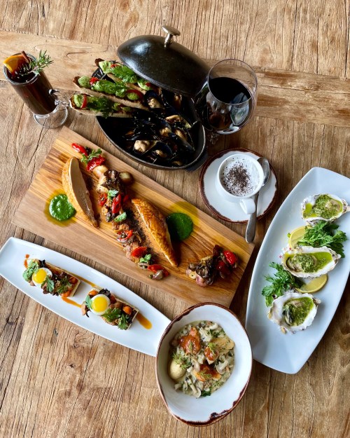A beautifully arranged seafood feast featuring grilled fish, oysters, mussels, and gourmet sides on a wooden table.