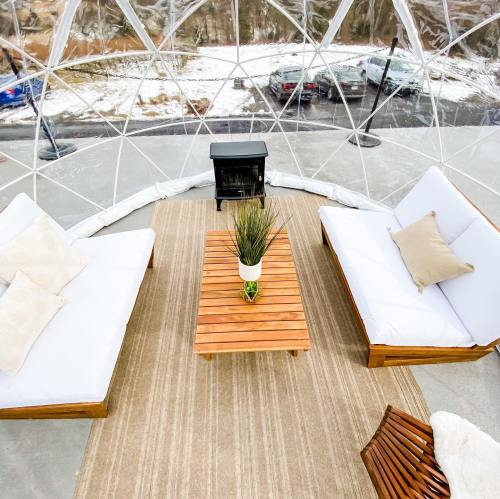 A cozy indoor space with a clear dome, featuring two white couches, a wooden table, and a small heater.