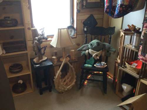 A cozy corner featuring a chair with a plush toy, a lamp, and various decorative items on shelves.