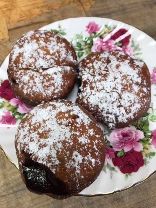 Three powdered sugar-dusted pastries on a floral plate, one with a bite taken out, revealing a chocolate filling.