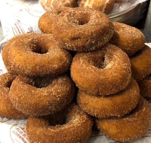A stack of freshly made, cinnamon-sugar coated donuts on a paper-lined tray.
