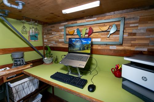 A cozy workspace featuring a laptop on a stand, keyboard, printer, and decorative birds on a wooden wall.