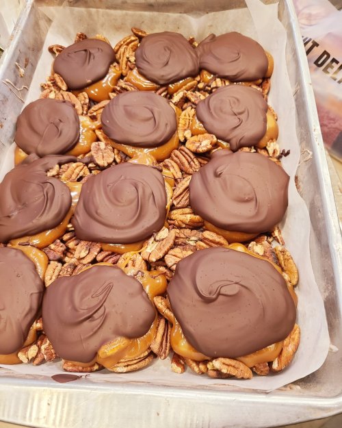 A tray of chocolate-covered caramel candies atop a bed of pecans, arranged neatly on parchment paper.