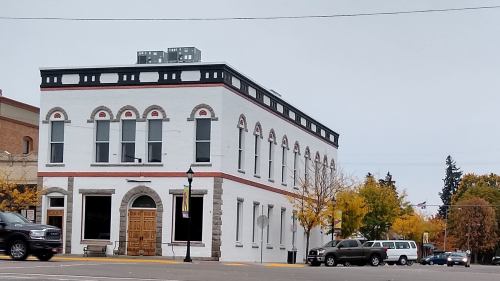 Historic white building with arched windows, red accents, and a wooden door, surrounded by autumn trees and parked cars.
