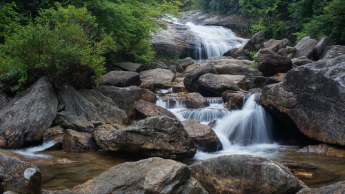 A serene waterfall cascades over rocks, surrounded by lush greenery in a tranquil natural setting.