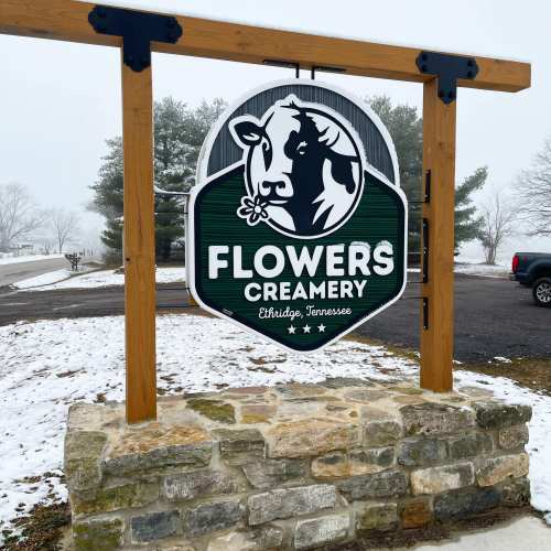Sign for Flowers Creamery in Ethridge, Tennessee, featuring a cow graphic and surrounded by a snowy landscape.