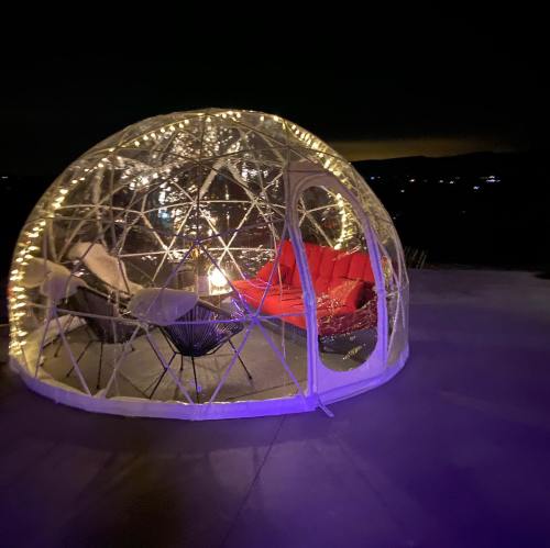 A cozy, illuminated geodesic dome with red seating and a fire pit, set against a night sky.