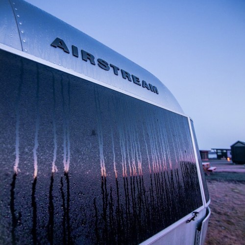 Close-up of an Airstream trailer with condensation on the window, set against a twilight sky.