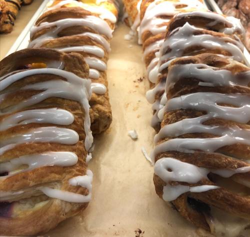 Two rows of flaky pastries drizzled with white icing, filled with fruit and cream, on a parchment-lined tray.
