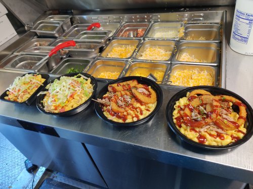 Four bowls of food featuring macaroni and cheese, topped with various ingredients, alongside a salad, in a food truck setting.
