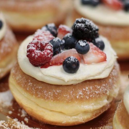 Close-up of a cream-filled donut topped with mixed berries and powdered sugar.