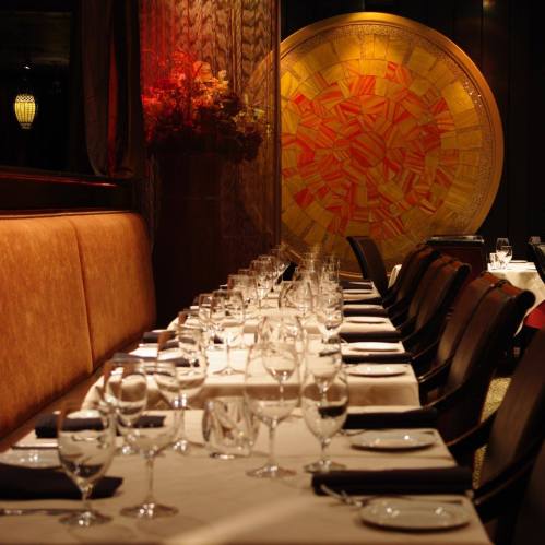 Elegant restaurant interior with a long table set for dining, featuring glassware and a vibrant decorative wall.