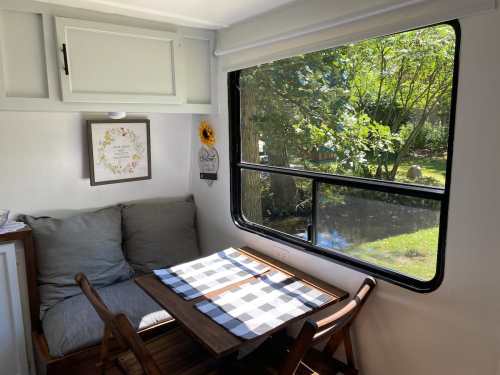 Cozy interior of a camper with a table, chairs, and a window showcasing greenery outside.