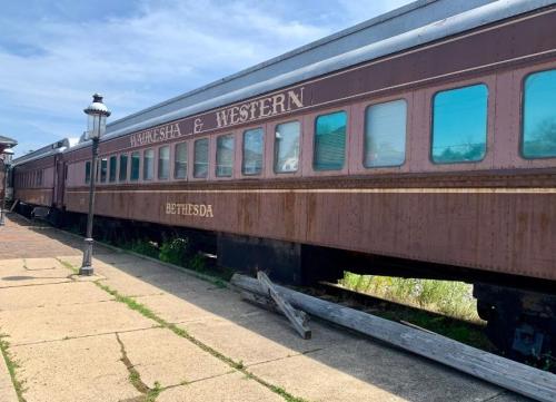 A vintage train car labeled "Waukesha & Western" parked beside a walkway on a sunny day.