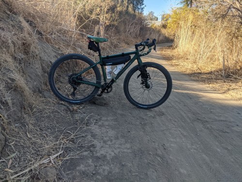 A green bicycle parked on a dirt trail surrounded by dry grass and sparse trees.