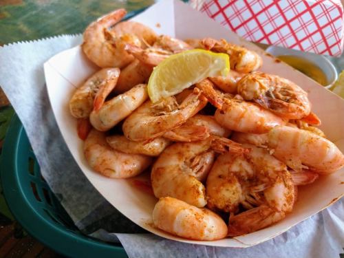 A basket of seasoned shrimp with a lemon wedge, served on a bed of parchment paper.