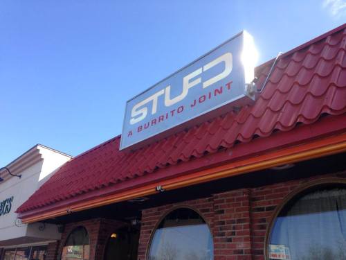 Sign for "STUFD: A Burrito Joint" on a building with a red roof and brick facade under a clear blue sky.