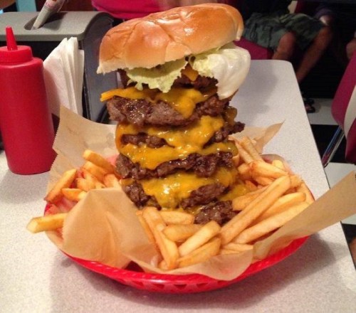 A towering burger with multiple beef patties and melted cheese, served with a side of golden French fries.
