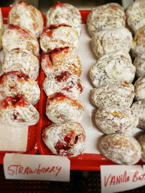 A display of powdered donuts filled with strawberry and vanilla cream, labeled accordingly on a red tray.
