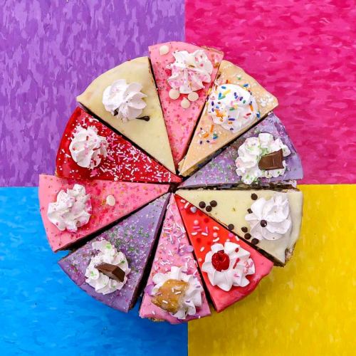A colorful assortment of cake slices topped with whipped cream, sprinkles, and cherries on a vibrant background.